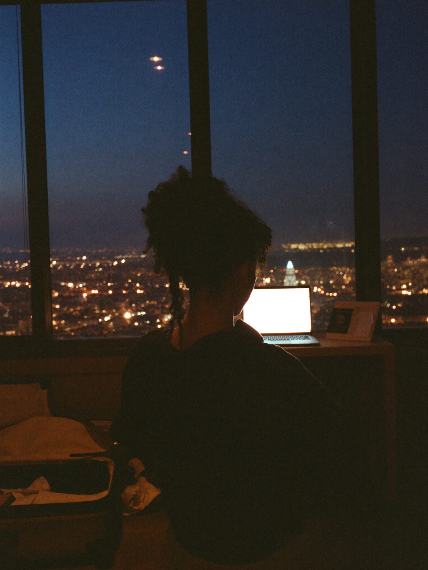 A desk at dusk with a laptop glowing beside a half-packed suitcase